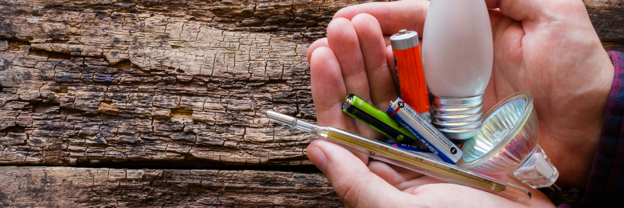 Universal waste of batteries, bulbs and thermometers held in hand with wood background